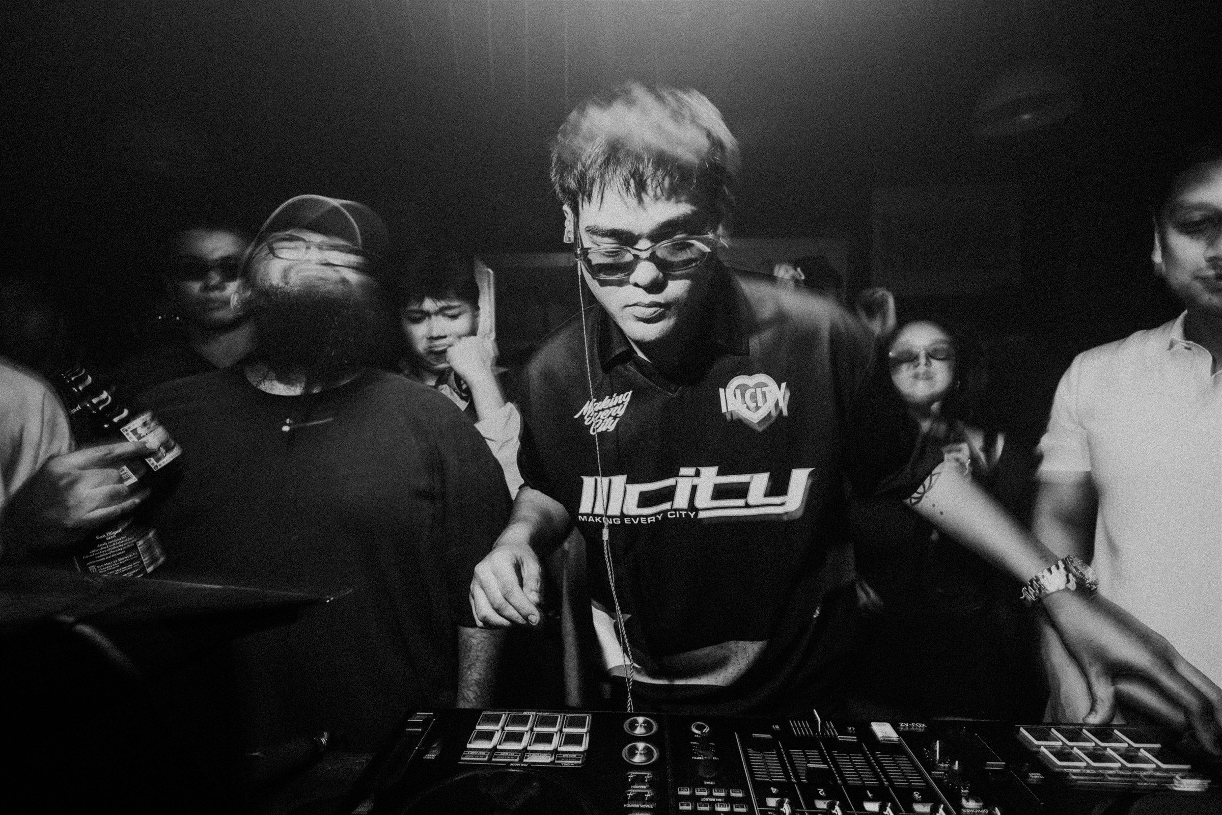 SPILLERS facing the crowd behind a DJ mixer, surrounded by guests in the club