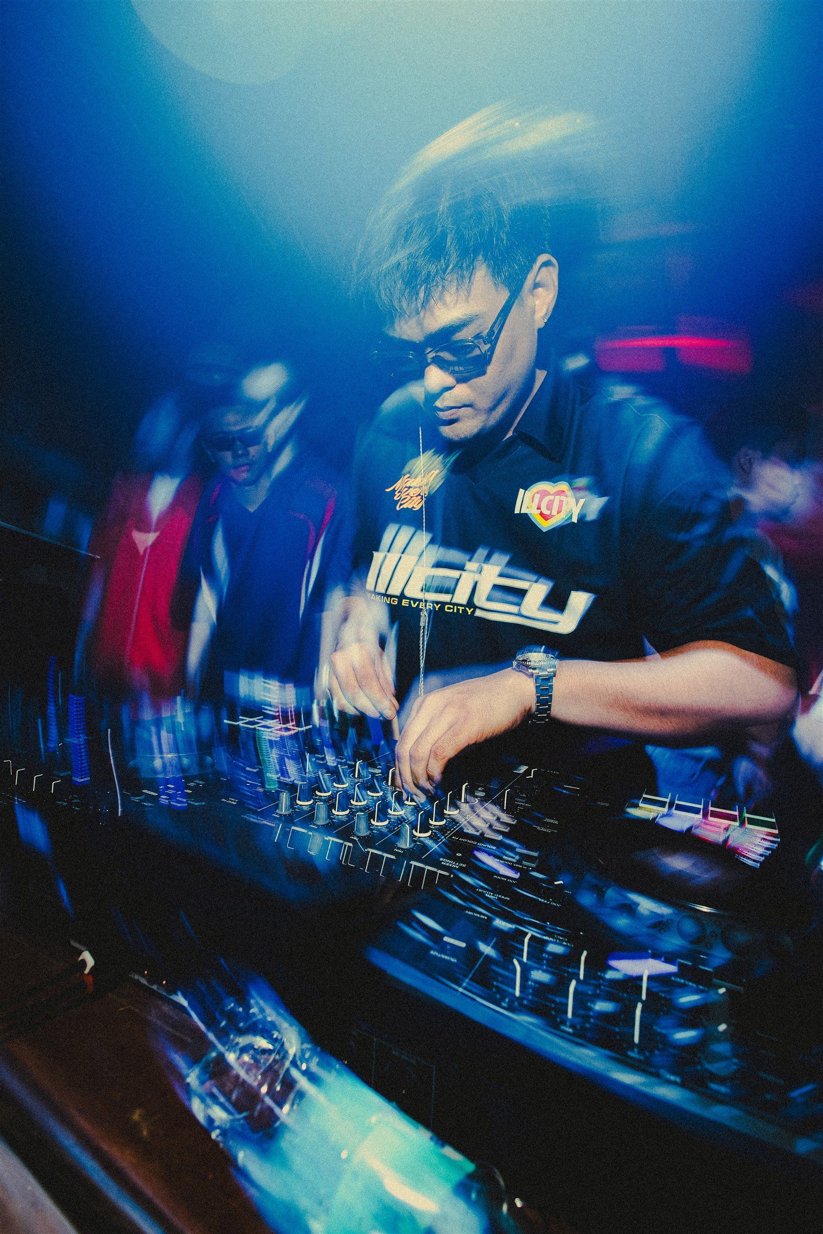 SPILLERS mixing on DJ decks under blue club lighting, with guests behind the booth