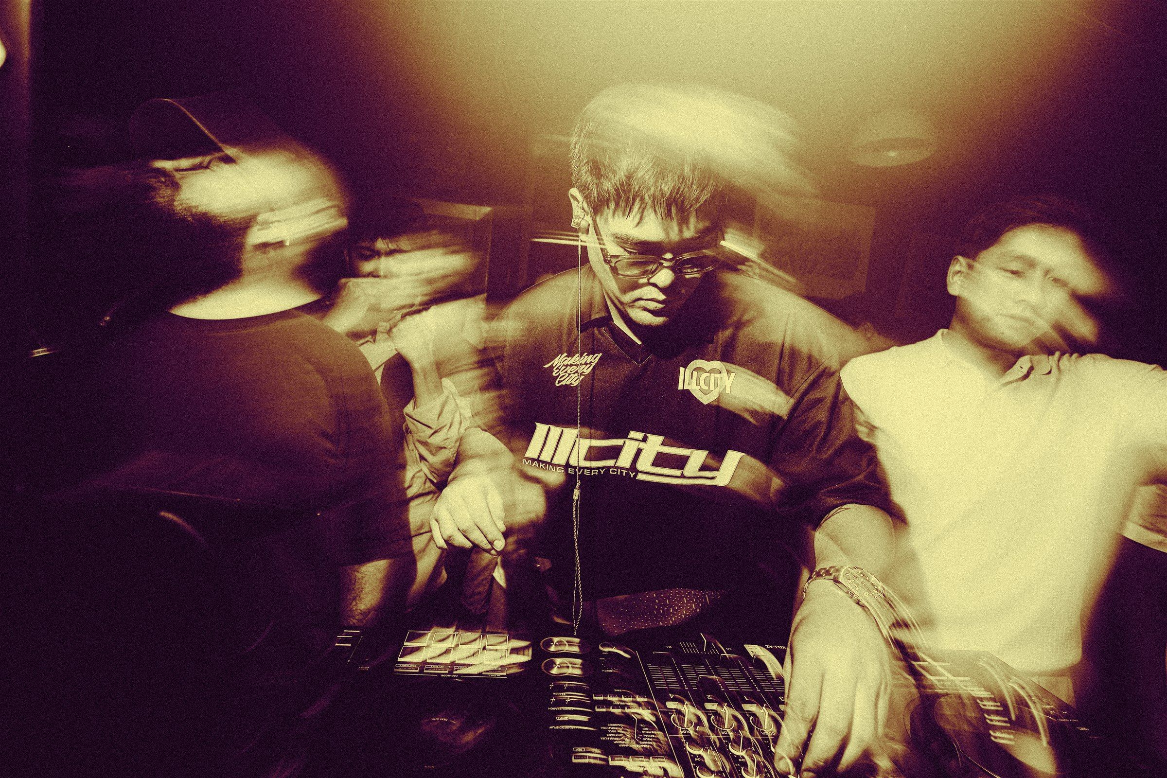 SPILLERS performing at the DJ mixer under warm club lighting, with guests in motion around the booth
